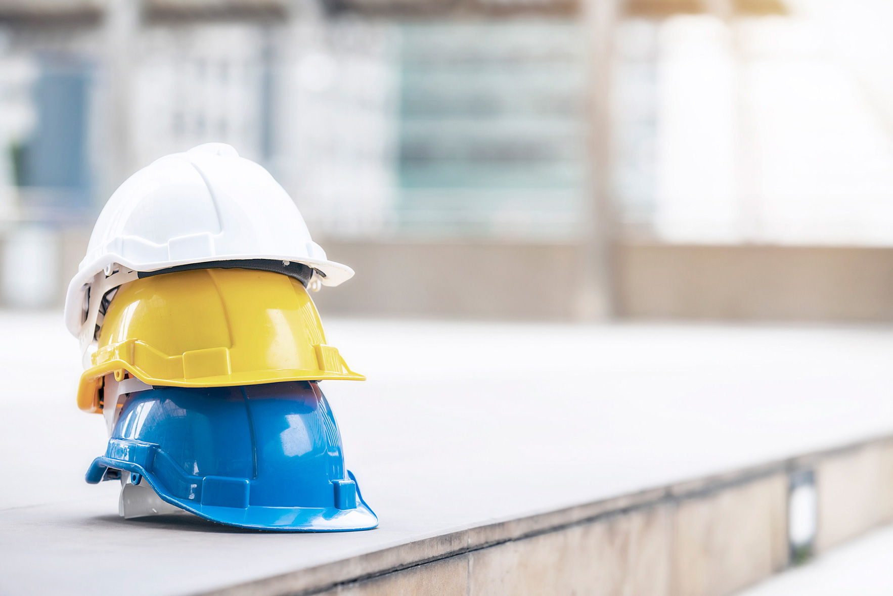 Hvit, gul og blå hard vernehjelm til arbeider, ingeniør eller besøkende liggende oppå hverandre på betonggulv i en by.